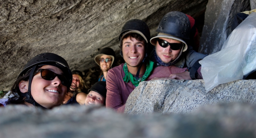 Six people smile at the camera while resting between boulders